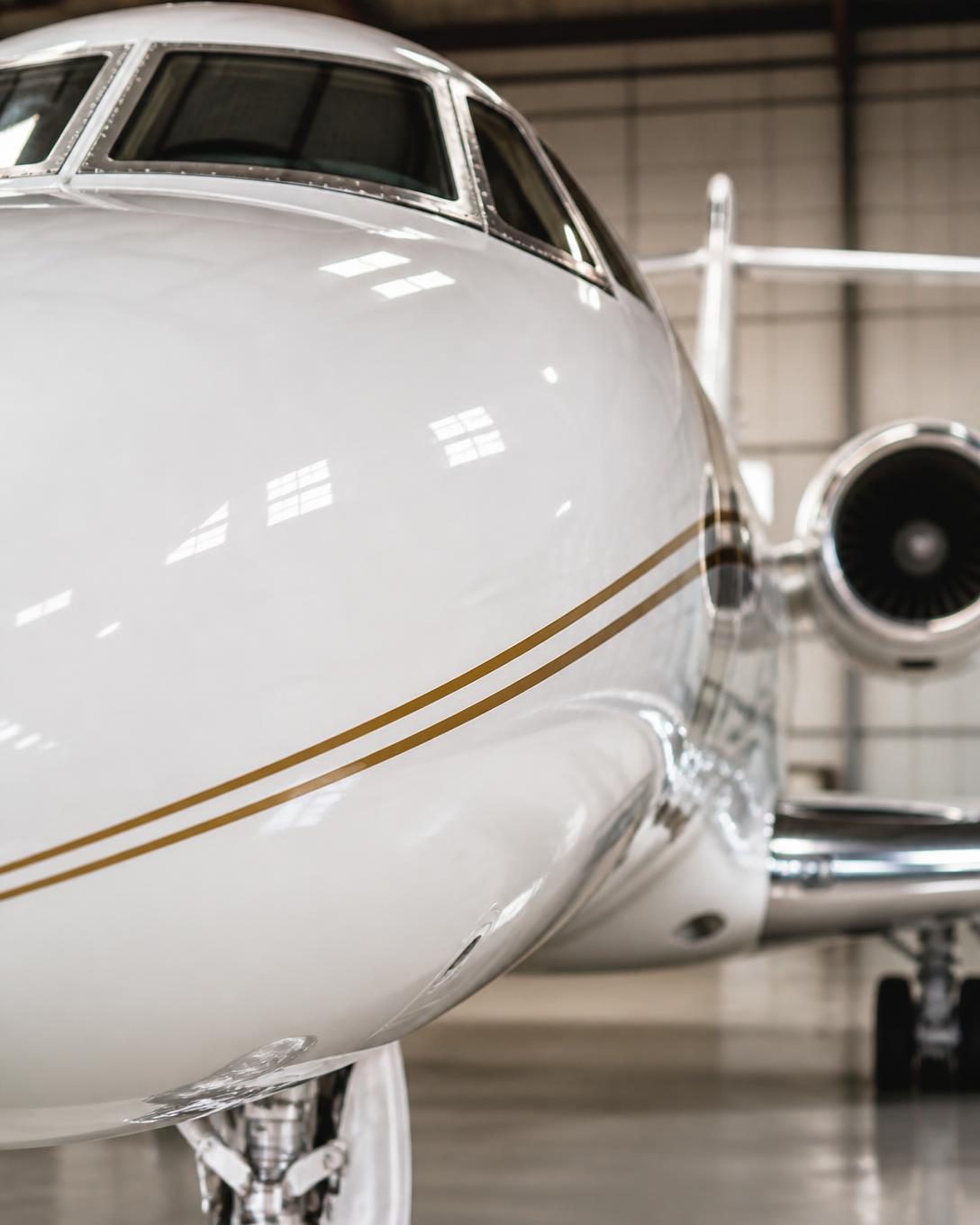 Freshly painted white private jet nose with a thin gold pinstripe